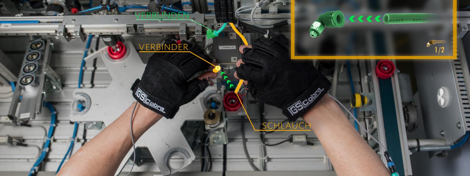 Handschubesetzte Arme führen eine Montagetätigkeit durch; zusätzliche Informationen werden überlagert eingeblendet
