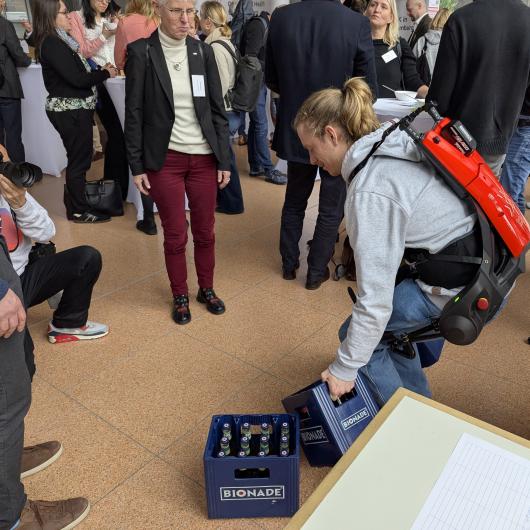 Exoskellett in Aktion beim Hochheben von Flaschenkisten mit Publikum