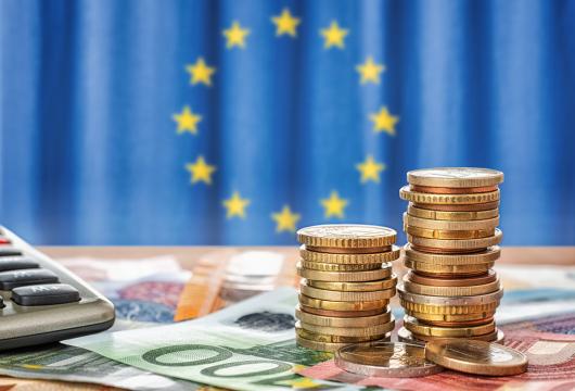 Finanzierungsmöglichkeiten Münzstapel und EU Flagge im Hintergrund